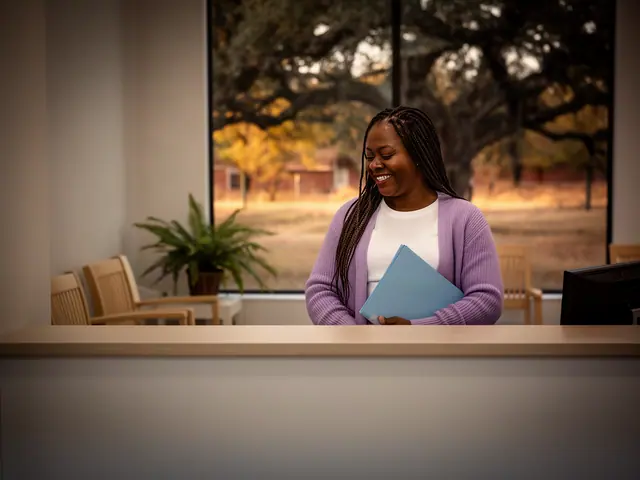 A clinic office manager holding a folder behind a reception counter.